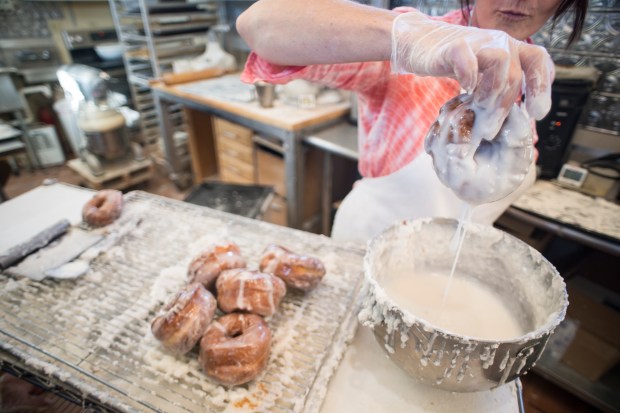 Nancy Martin dips a warm doughnut in glaze at Windmill Village Bakery in Ravalli, Montana.