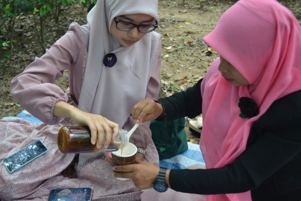 Indonesian women carefully pour palm sugar into a cup of ice and coconut milk, making cendol.