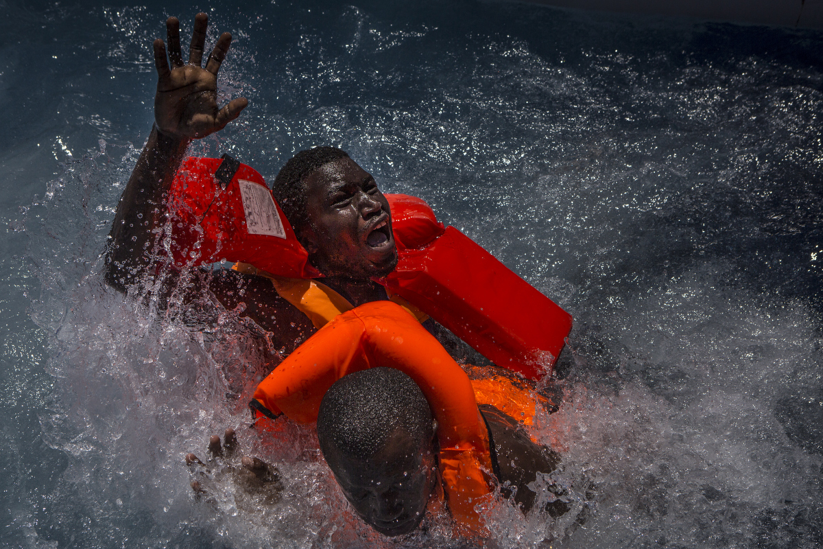 Two men panic after their rubber boat deflated, tipping many migrants into the water.