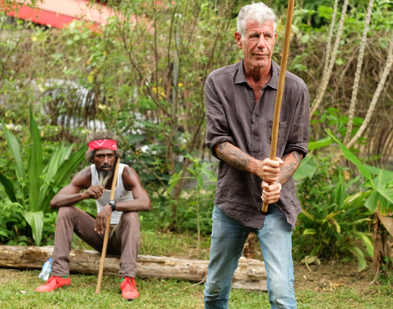 King David looks on as Bourdain takes a turn at stick fighting.