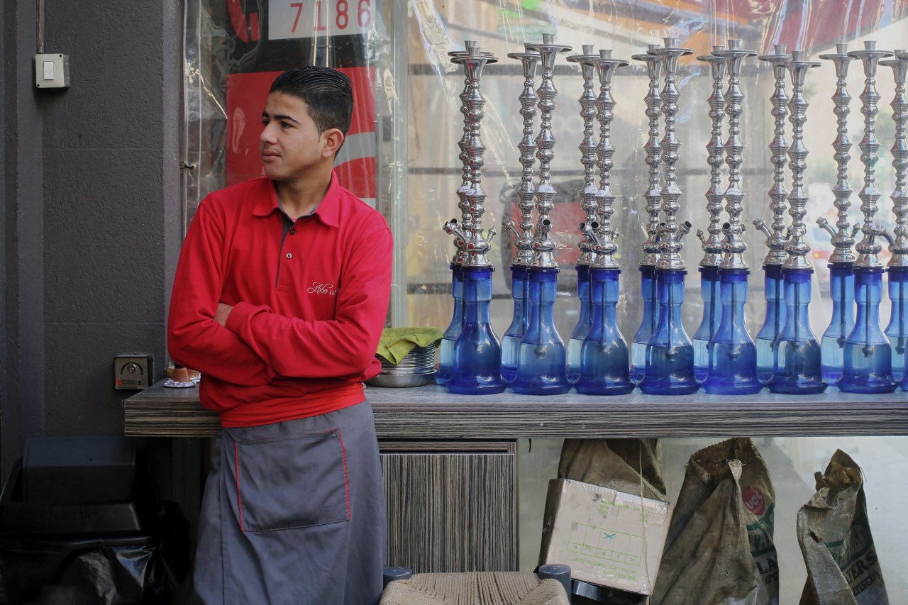 A Syrian employee of the restaurant stands next to hookah pipes.