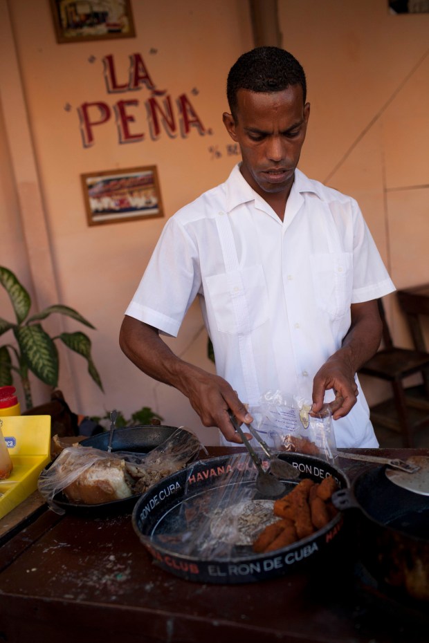 A Cuban man serves croquettes from a tray in a small local cafe, Havana old town. (Photo by In Pictures Ltd./Corbis via Getty Images)