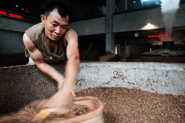 Photo 1: A worker sifts through a vat of grains at the museum production area. The museum is dedicated to the history and culture of this quintessential Chinese spirit. Photo 2: Workers add Qu, or starter culture, to a mash of grains at the museum production area. Baijiu recipes vary widely and include grains like sorghum, rice, corn and wheat.